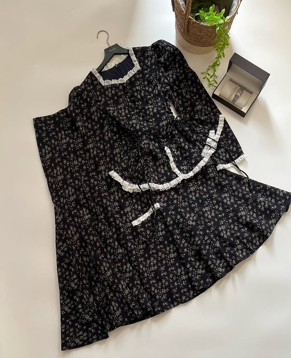 Vintage-inspired black floral modest two-piece set with white lace trim and long sleeves laid on clean studio background.